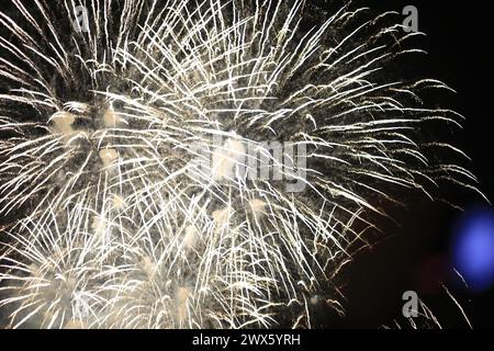 Weißes Feuerwerk stürzt vor einem dunklen Himmel mit einem Hauch von blauem Licht Stockfoto