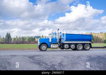 Leistungsstarker Industrieträger blauer Kipper-Sattelzugmaschine mit zwei Kippanhängern für den Transport von Fracht auf der Autobahn an sonnigen Tagen Stockfoto