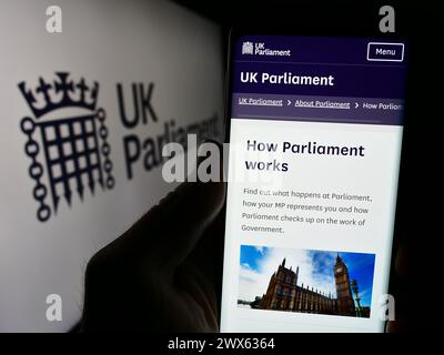 Person, die ein Mobiltelefon hält, mit Webseite des Legislative Body Parliament of the United Kingdom (UK) mit Logo. Konzentrieren Sie sich auf die Mitte des Telefondisplays. Stockfoto