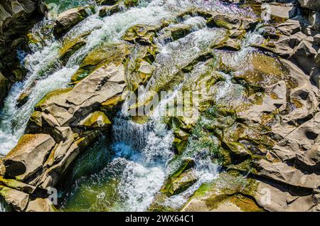 Blick von oben auf einen Teil eines Bergflusses mit einem kleinen Wasserfall an einem rauen Sommertag Stockfoto