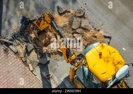 Bagger gräbt Asphalt, um eine Wasserstörung in einer Straße zu reparieren Stockfoto