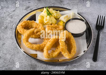 Gebratene Calamari mit Kartoffelsalat daneben auf Steintisch Stockfoto