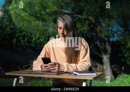 Frau, die draußen in der Natur arbeitet, mit ihrem Handy und ihrem Schreibtisch Stockfoto