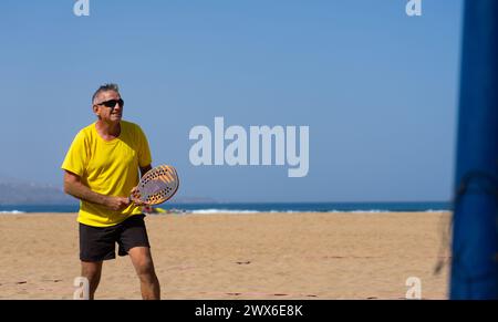 Ein älterer Herr spielt Strandtennis. Seniorenmann mit gesundem Lebensstil Stockfoto