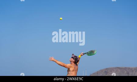Reifer Mann, der Strandtennis serviert Stockfoto