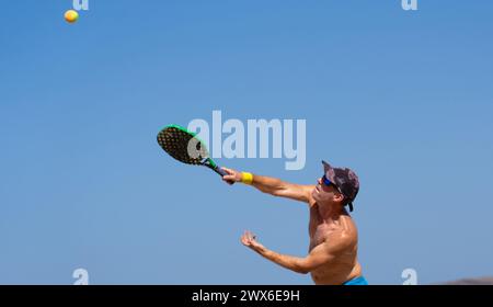 Reifer Mann, der einen Strandtennis macht, mit blauem Himmel im Hintergrund und Kopierraum Stockfoto