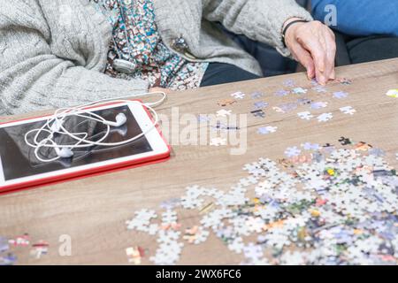 Die Hand einer älteren Frau macht ein Puzzle und eine Tablette am Tisch Stockfoto