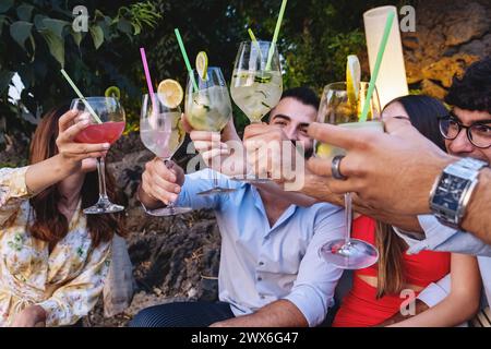 Lebhafte Gruppe mit jungen Erwachsenen, die mit Cocktails anstoßen - Naturfeier, erfrischende Sommergetränke - Millennials lebhafte Outdoor-Applaus, fröhliche Momen Stockfoto