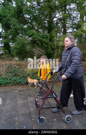 Großmutterfamilie mit ihrem Enkel und ihrem Hund, die zusammen laufen, Großmutter mit einem Walker Stockfoto