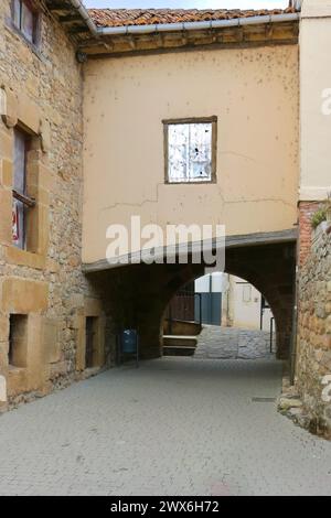 Historisches Stadtsteintor unter einem schrägen Gebäude und niedriger Bogen Calle de Puente y Puerta de San Roque Aguilar de Campoo Palencia Castile und Leon Spanien Stockfoto