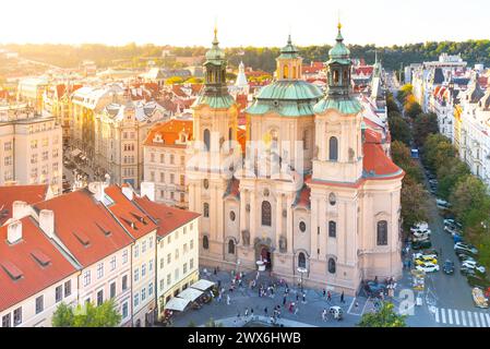 Das goldene Sonnenlicht taucht die Nikolaikirche und umgibt den Altstadtplatz, der die barocke Architektur hervorhebt und warme Töne über dem belebten Stadtplatz ausstrahlt. Prag, Tschechien Stockfoto