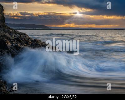 Wellen brechen bei Flut auf den zerklüfteten Felsen entlang des Küstenwanderweges an der Flussmündung des River Torridge von Appledore ab und blicken in Richtung Westen H Stockfoto