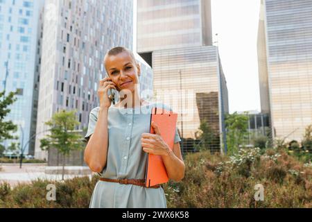 Eine Geschäftsfrau, die in einer städtischen Grünfläche steht. Stockfoto