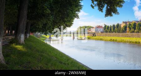 uschgorod, ukraine - 4. juni 2017: Altstadt mit Fluss. Damm mit Linden in Blüte. Brücke und alte Gebäude in der Ferne am Morgen Long Stockfoto
