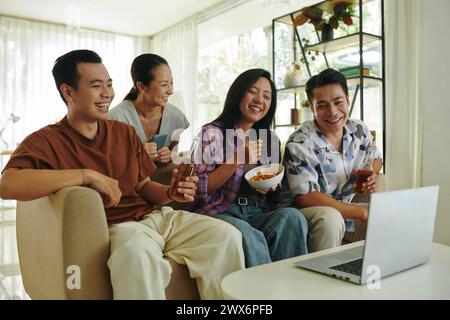 Eine Gruppe von Freunden versammelte sich vor dem Laptop, um Getränke zu trinken und eine Comedy-Show zu sehen Stockfoto