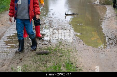 Kinder in Gummistiefeln, die durch eine schlammige Pfütze laufen Stockfoto