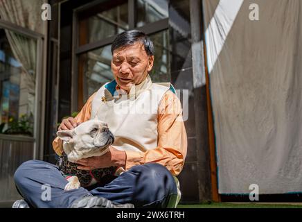 (240328) -- LHASA, 28. März 2024 (Xinhua) -- Phutsering spielt mit einem Hund zu Hause in Lhasa, südwestchinesischer Autonomen Region Xizang, 23. März 2024. Phutsering wurde 1944 in Bainang County der Stadt Xigaze geboren und wuchs in einer ehemaligen Serfenfamilie auf. Eine bescheidene Hütte in der Nähe des Herrenhauses, wo seine Mutter als Leibeigene arbeitete, diente als Heim seiner Kindheit. Währenddessen kämpfte sein Vater, der in einem separaten Herrenhaus beschäftigt war, mit Landwirtschaft und Handwerk während der mageren Monate um die Runden zu kommen, und erzielte kaum ein ausreichendes Einkommen, um die Miete und Steuern für ihre Wohnungen und Felder zu decken. Mit 13 Jahren war er gr Stockfoto