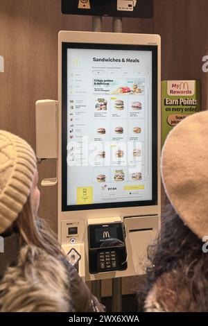 Nueva York, USA - 28. März 2024: Das Bild zeigt zwei Kunden, die einen Selbstbedienungskiosk bei einem McDonald's. Sie interagieren mit einem großen Touch sc Stockfoto