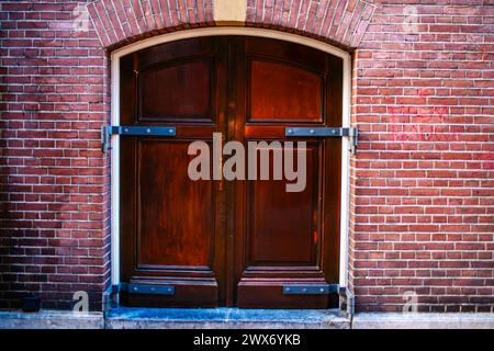 Eine Vintage-Tür ziert eine strukturierte Backsteinmauer in einer Amsterdamer Straße, die architektonischen Charme mit verwittertem urbanen Charme verbindet. Stockfoto