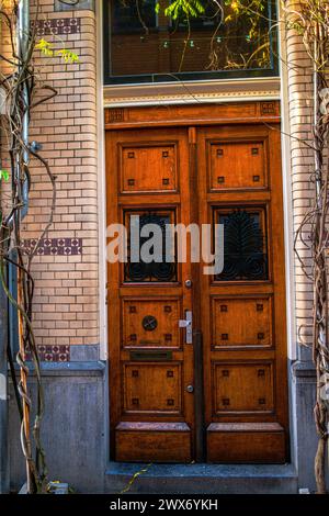 Eine Vintage-Tür ziert eine strukturierte Backsteinmauer in einer Amsterdamer Straße, die architektonischen Charme mit verwittertem urbanen Charme verbindet. Stockfoto