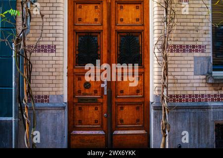 Eine Vintage-Tür ziert eine strukturierte Backsteinmauer in einer Amsterdamer Straße, die architektonischen Charme mit verwittertem urbanen Charme verbindet. Stockfoto