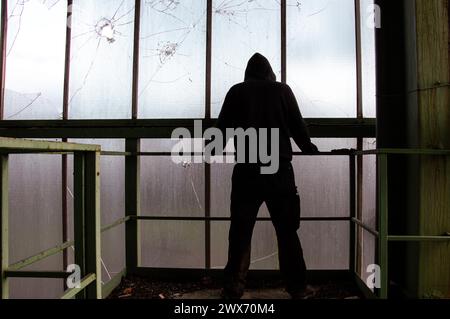 Eine geheimnisvolle Figur mit Kapuze, zurück zur Kamera, in einem verlassenen Industriebau Stockfoto