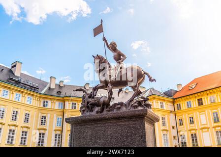 Die Bronzestatue des Heiligen Georg tötet triumphierend einen Drachen vor der pulsierenden Kulisse der Prager Burg unter blauem Himmel. Prag, Tschechien Stockfoto