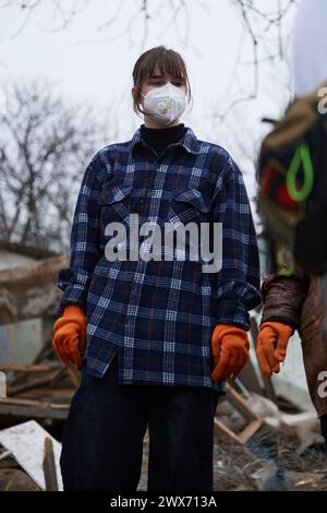 Porträt eines jungen ukrainischen Freiwilligen, der Maske und Handschuhe trägt, während er Müll an der Absturzstelle aufnimmt. Kiew - 23. März 2024 Stockfoto