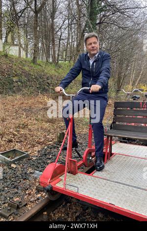 Malente, Deutschland. März 2024. Bundeswirtschaftsminister Robert Habeck erfährt von der Nutzung einer stillgelegten Eisenbahnstrecke in Schleswig-Holstein als wissenschaftliches Praxislabor für den Nahverkehr der Zukunft. Habeck löst mit einem Wagen eine Barriere aus. Quelle: Sönke Möhl/dpa/Alamy Live News Stockfoto