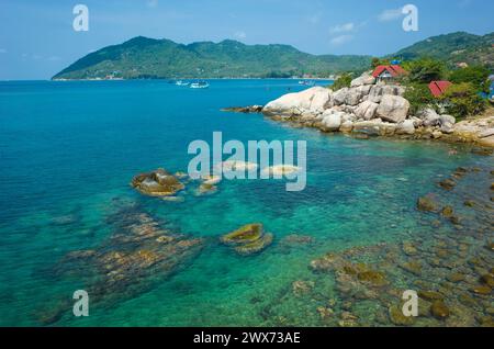 Urlaub auf tropischen Inseln, Küste von Koh Tao Insel mit türkisfarbenem, klarem Meerwasser, felsigem Boden, Häusern mit rotem Dach hinter Granitfelsen. Beliebt Stockfoto