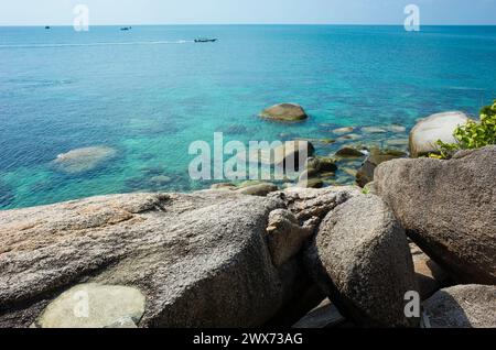 Tropische Inselküste mit türkisfarbenem klarem Wasser, felsigem Boden, Felsbrocken, Boot im offenen Meer. Koh Tao Insel ist ein beliebtes Reiseziel Stockfoto