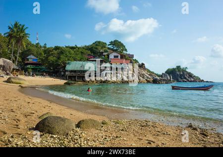 Korallensand am kleinen Sai Nuan Strand auf der tropischen Insel Koh Tao, beliebtes Reiseziel für Thailand. Bungalows auf Klippen und Boot auf Wasser Stockfoto