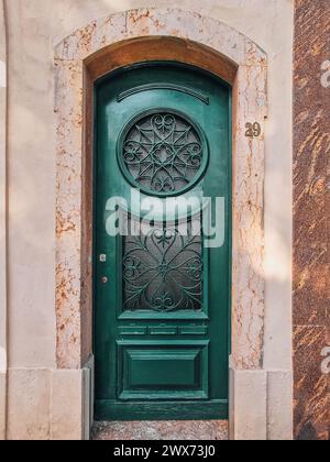 Fassade des alten Hauses mit grüner Holztür, verziert mit Milchglas und dekorativen Schmiedemustern. Alte Tür in Portugal gefunden Stockfoto