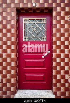 Fassade eines restaurierten alten Hauses mit Vintage-braunen Fliesen an den Wänden und einer Holztür in leuchtendem Rot mit dekorativer Metallluke Stockfoto