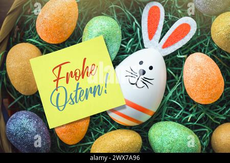 FOTOMONTAGE, Osterhasen-Osterei und Zettel mit Aufschrift Frohe Ostern in einem Osternest *** FOTOMONTAGE, Osterhasen-Osterei und Notiz mit der Aufschrift Frohe Easter in a Easter Nest Stockfoto