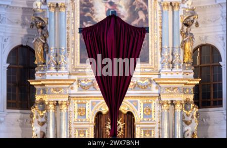 München, Deutschland. März 2024. Ein rotes Tuch bedeckt das Kreuz vor dem Altar in St. Michaels Kirche. In vielen Kirchen werden im Vorfeld von Ostern Jesu Darstellungen verschleiert, um dann am Karfreitag in einem Gottesdienst wieder feierlich enthüllt zu werden. Quelle: Sven Hoppe/dpa/Alamy Live News Stockfoto