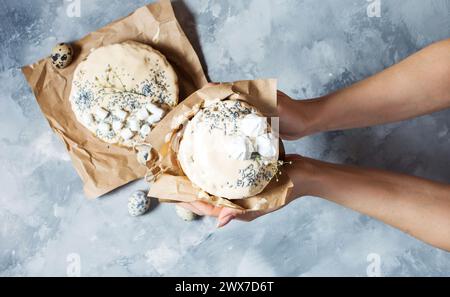 Weibliche Hände halten den Osterkuchen auf einem grauen Betontisch. Frühlingsferien. Draufsicht. Stockfoto
