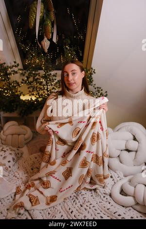 Junge, schöne lächelnde Frau, die im Bett mit einem Kuchenmann auf der Verpackung mit weißem Pullover im Zimmer liegt, das für die Feier des neuen Jahres und weihnachten eingerichtet wurde Stockfoto