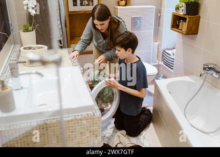 Teenager-Mädchen hilft dem Bruder beim Laden von Kleidung in die Waschmaschine zu Hause Stockfoto