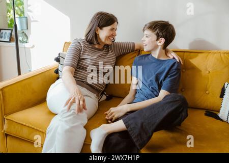 Lächelnde Frau, die mit dem Sohn spricht, während sie zu Hause auf dem Sofa sitzt Stockfoto