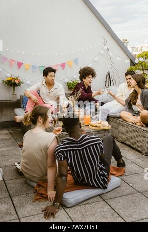 Eine Gruppe glücklicher multirassischer Freunde, die während der Party auf dem Balkon sitzen Stockfoto