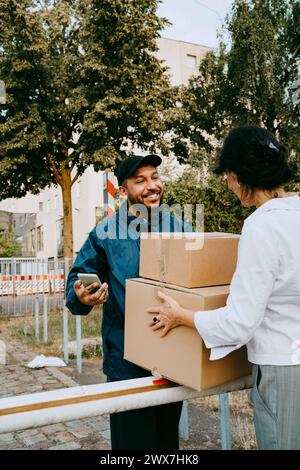 Lächelnder männlicher Lieferer, der mit der Frau spricht, während er Pakete zustellt Stockfoto