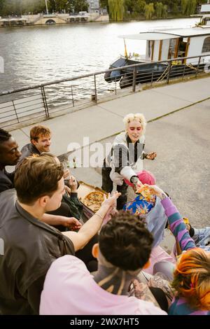 Blick auf nicht-binäre Freunde, die Pizza in der Nähe der Promenade in der Stadt teilen Stockfoto