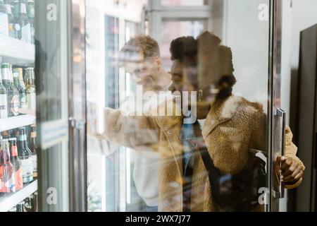 Aufgeregt, junge Frau, die Getränke aus dem Kühlbereich kauft, während sie mit ihrem Freund im Supermarkt shoppt Stockfoto
