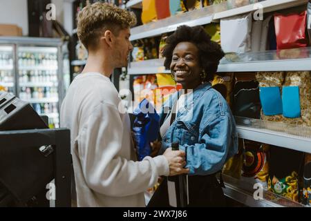 Lächelnde junge Frau, die mit ihrem Freund einkaufen geht, während sie am Gang im Supermarkt steht Stockfoto