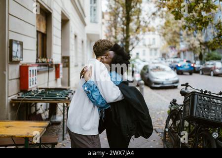 Seitenansicht eines Mannes, der eine multirassische Freundin umschließt, während er auf dem Bürgersteig in der Stadt steht Stockfoto