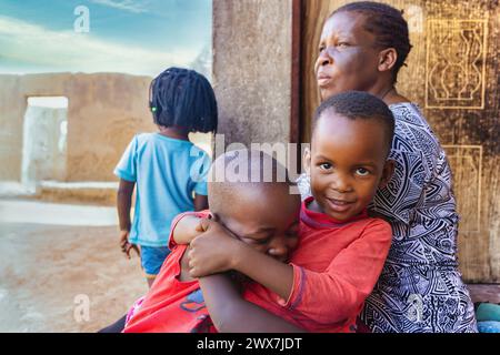 Nur wenige afrikanische Kinder spielen und streiten auf der Veranda vor dem Haus, Oma beobachtet, afrikanisches Dorfleben Stockfoto