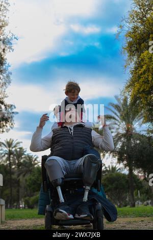 Als inklusives Familienmitglied spielen sie im Park, für den Vater ist es kein Problem, beide Beine verloren zu haben und im Rollstuhl zu sitzen. Stockfoto