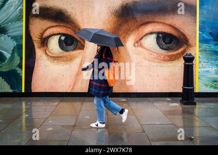 London, Großbritannien. 28. März 2024. Wetter in Großbritannien – Eine Frau, die Kunstbauten durchläuft, die vor der National Gallery am Trafalgar Square während zeitweiliger Regengüsse hortet, da die Auswirkungen des Sturms Nelson in der Hauptstadt zu spüren sind. Die Prognose für das Osterwochenende sieht mehr unruhige Bedingungen vor. Quelle: Stephen Chung / Alamy Live News Stockfoto