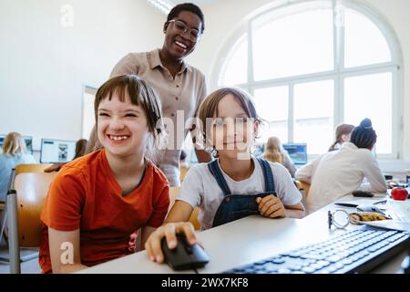 Porträt eines lächelnden Mädchens neben einer behinderten Freundin im Computerunterricht in der Schule Stockfoto